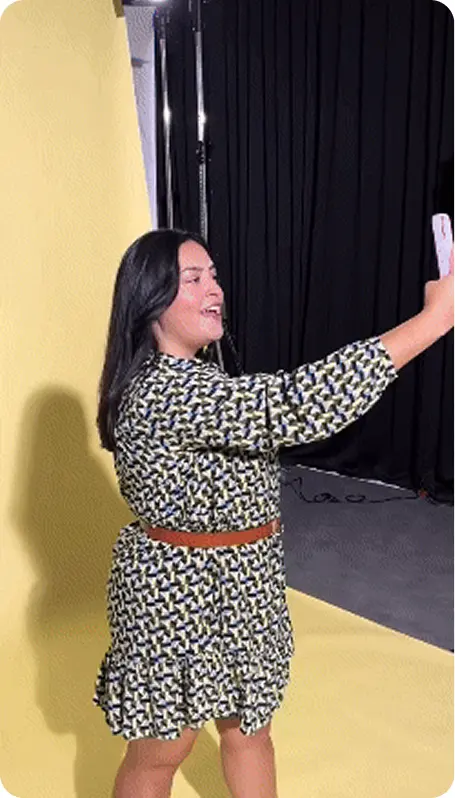 A behind the scenes photo of a momox fashion social media video shooting showing a woman in a momox fashion outfit taking a selfie of herself in front of a yellow canvas